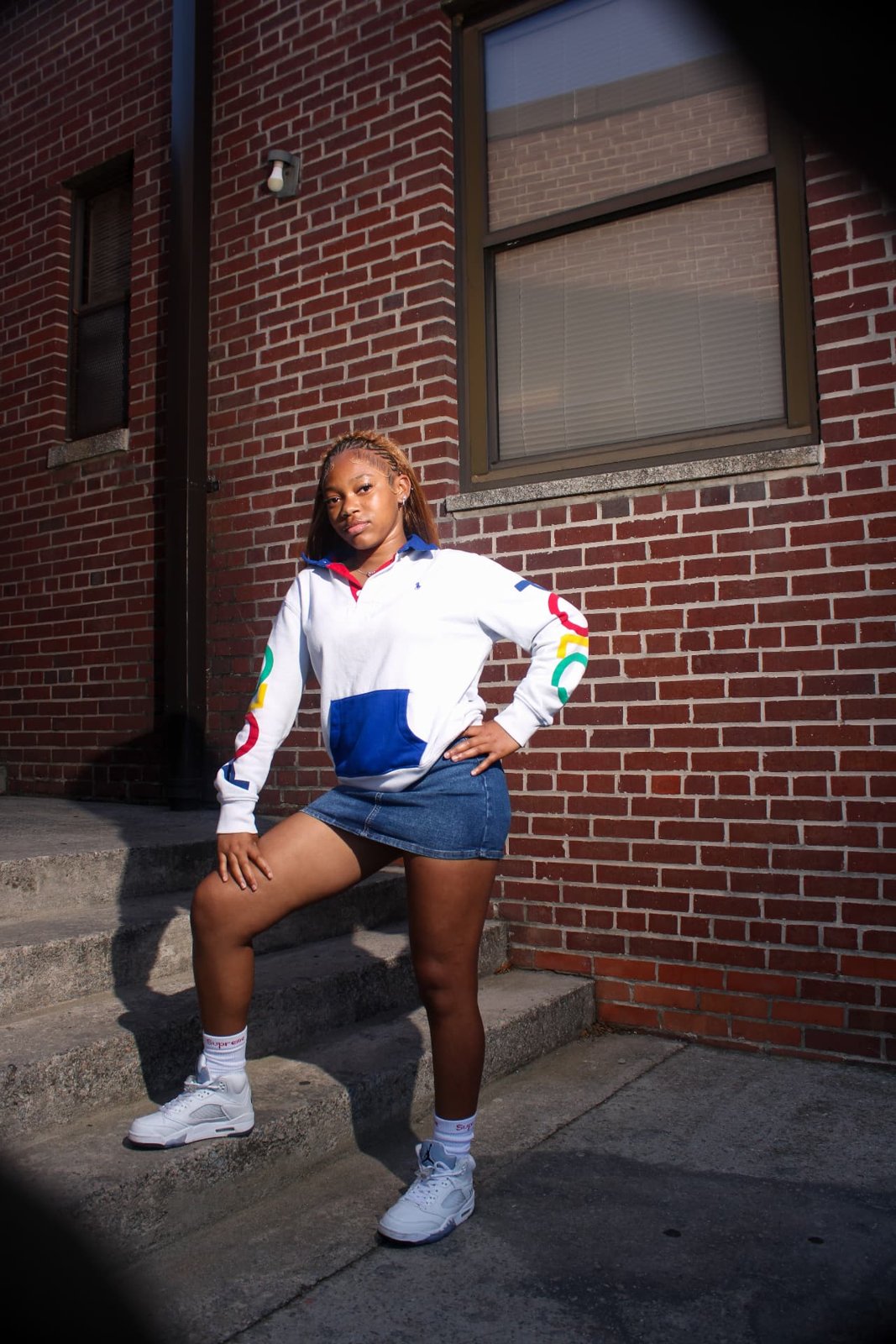 Woman in a colorful rugby shirt and denim skirt posing on brick building steps