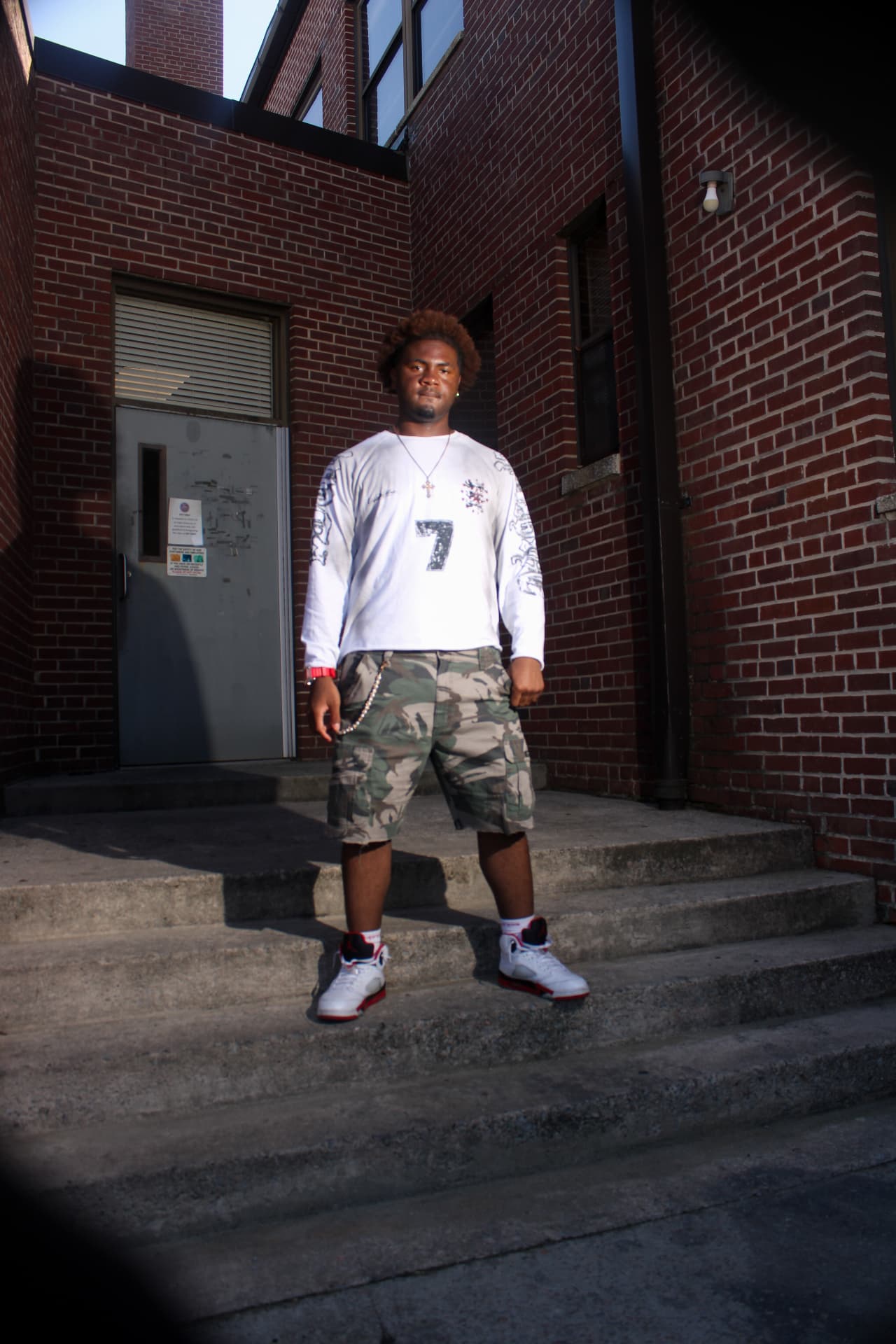 isaiahvzn standing on concrete steps outside a red brick building, facing the camera