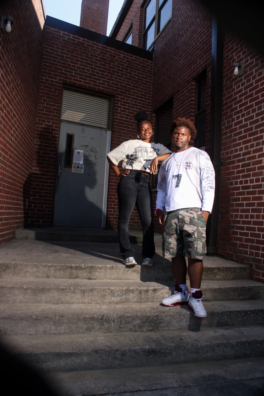 Two friends in streetwear standing on steps outside a brick building