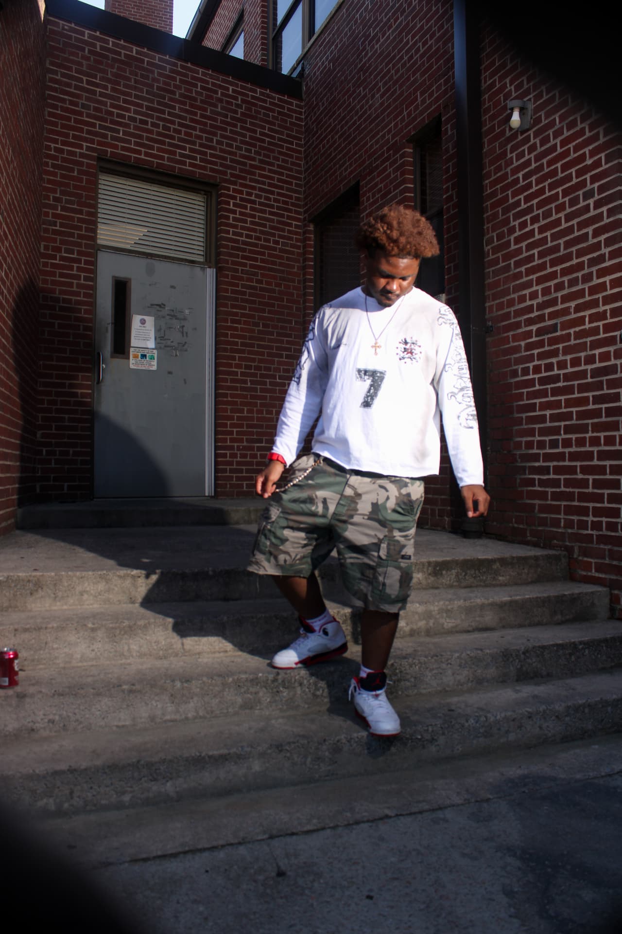 isaiahvzn looking down at the steps as he walks outside a red brick building